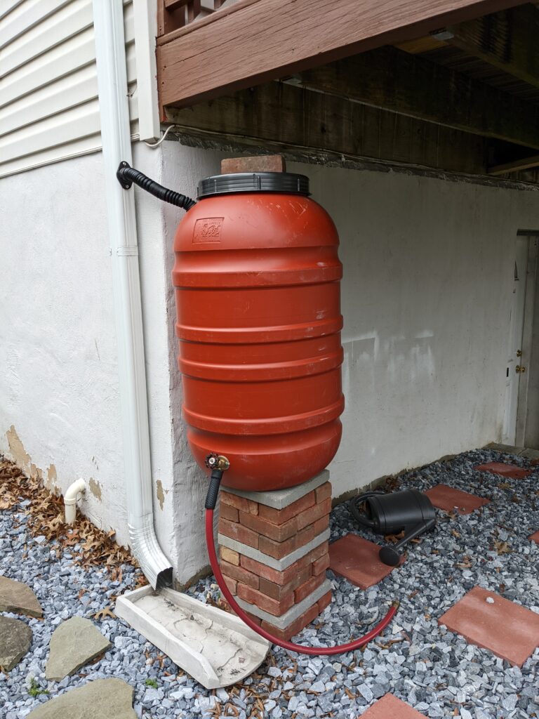 Rote Regentonne am Fallrohr zum Sammeln von Regenwasser für die Gartenbewässerung